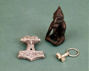 Amuletos de deidades vikingas: en primer plano dos pequeños martillos de plata que simbolizan al dios Thor. La estatuilla representa a Freyr, dios de la fertilidad. Museo Histórico de Estocolmo, Suecia.