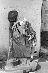 Niña vaciando un cubo de agua en una fuente, 9 de mayo de 1939 (foto b/n)