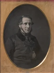 Hombre de mediana edad con barba de correa, mano metida dentro de la chaqueta abotonada, 1840s-50s