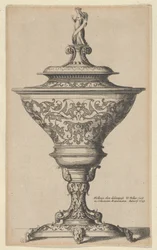 Copa ornamentada sobre pies de máscaras