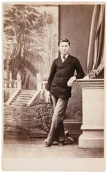Retrato de estudio de un joven frente a un fondo pintado de escaleras y jardín