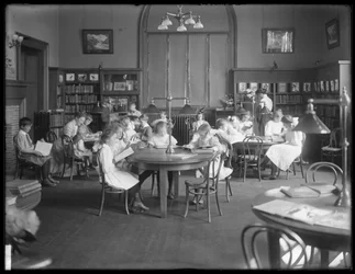 Niños leyendo en la sala de lectura de una sucursal no identificada de la Biblioteca Pública del Borough de Queens, c.1910