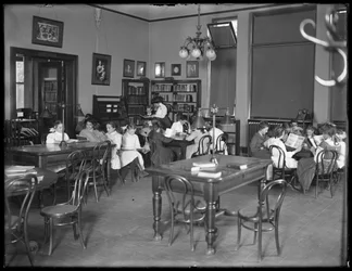 Niños leyendo en la sala de lectura de una sucursal no identificada de la Biblioteca Pública del Borough de Queens, c.1910