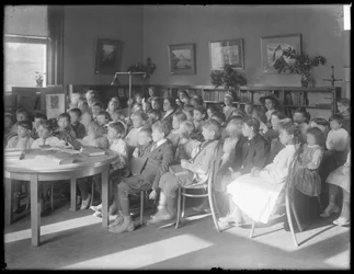 Niños sentados, escuchando en la sala de lectura de una sucursal no identificada de la Biblioteca Pública del Distrito de Queens, c.1910