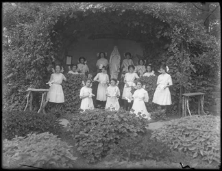 Clase graduada de niñas del Asilo de Huérfanos Católicos Romanos posando frente a la gruta con sus diplomas, 1912