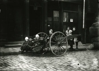 Grupo de niños en un carro, con una niña y una mujer de pie detrás, c.1910-21
