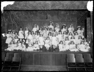 Grupo de niñas pequeñas posando en un pequeño escenario sosteniendo muñecas, probablemente el Asilo de Huérfanos Católicos Romanos, Kingsbridge, Bronx, c.1911