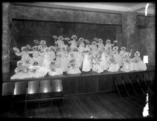 Grupo de niñas pequeñas posando en un pequeño escenario con abanicos, probablemente el Orfanato Católico Romano, Kingsbridge, Bronx, c.1911