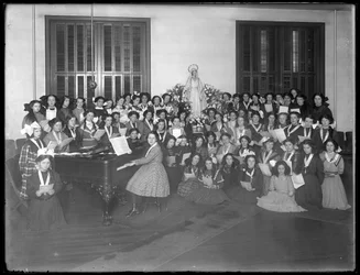Retrato grupal de una clase de coro de niñas reunidas alrededor de un piano con partituras, probablemente en el Asilo de Huérfanos Católicos Romanos en Kingsbridge, Bronx, c.1911
