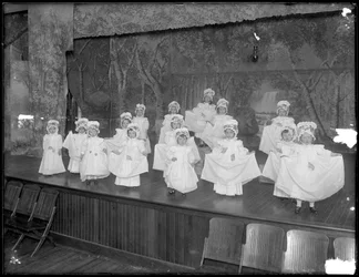 Niños de jardín de infantes en el escenario: niñas muy pequeñas actúan en un pequeño escenario, probablemente el Asilo de Huérfanos Católico Romano, Kingsbridge, Bronx, c.1911