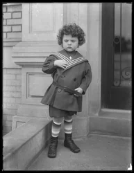 Niño pequeño con traje de marinero en la entrada del edificio de apartamentos de la Avenida Vermilyea, c.1913