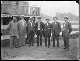 Siete hombres no identificados posan cerca de un río o lago, c.1910