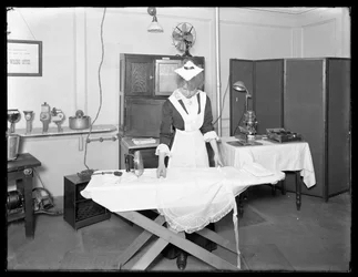 Joven mujer en traje de sirvienta demostrando el uso de una plancha eléctrica, c.1913-14